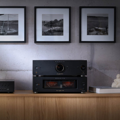 Black audio equipment on a wooden shelf with framed black and white photos on the wall.