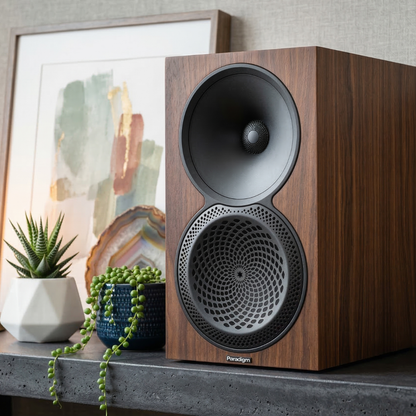 Wooden speaker on a shelf with decorative items and a framed picture in the background