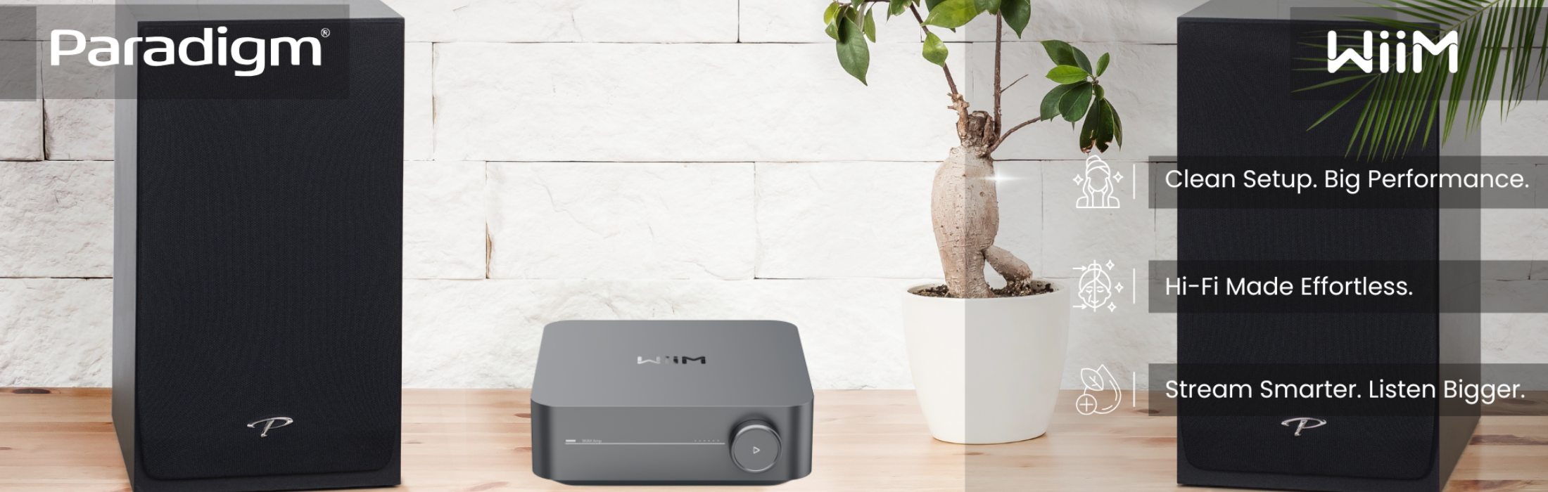 Three electronic devices on a wooden surface with a white brick wall and plant in the background.