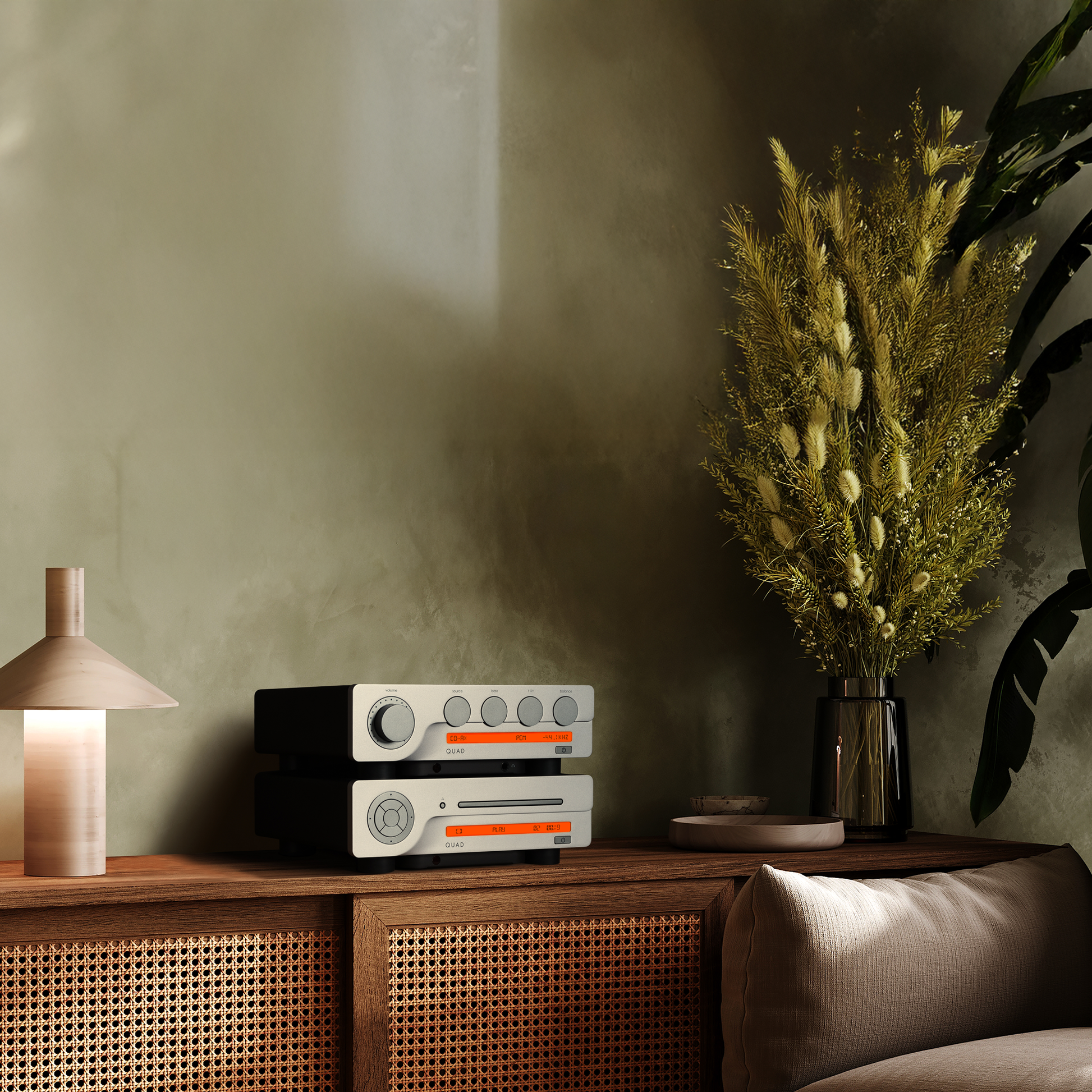 Stack of electronic devices on a wooden cabinet with a plant and lamp in the background.
