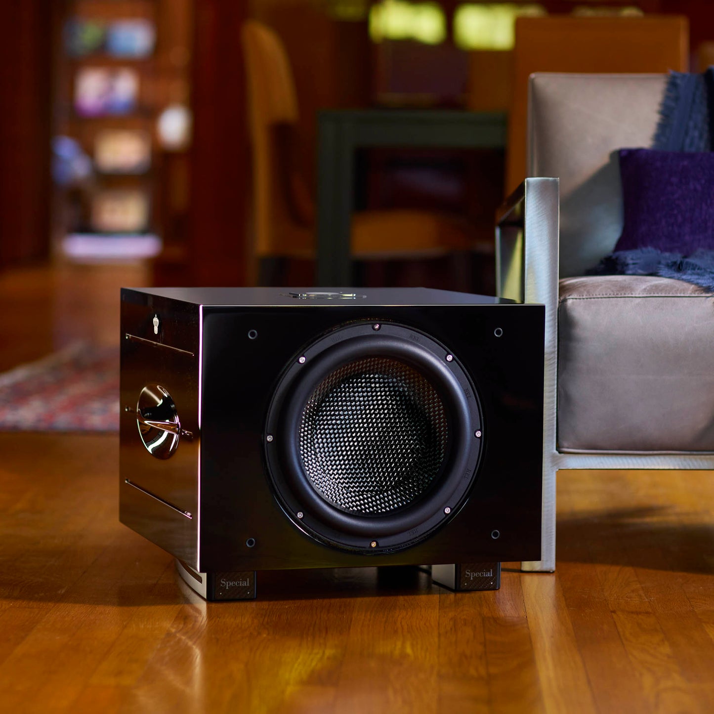 Black subwoofer on a wooden floor with a blurred living room background