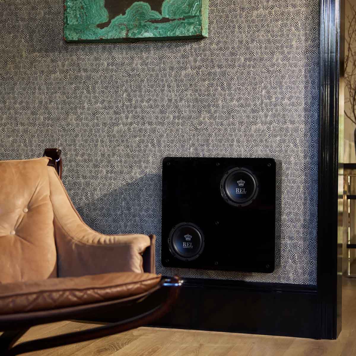 Black subwoofer mounted on a textured wall next to a brown armchair.