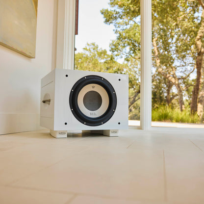 White subwoofer in front of a glass door with a view of trees outside