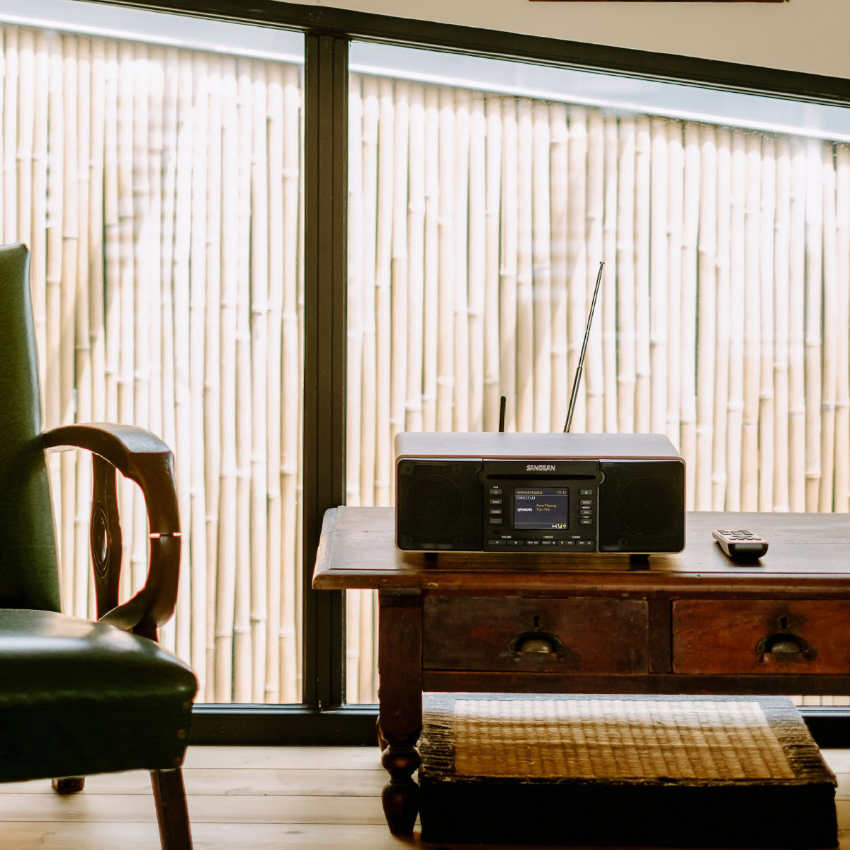 Radio on a wooden table with a green chair and sliding glass door in the background