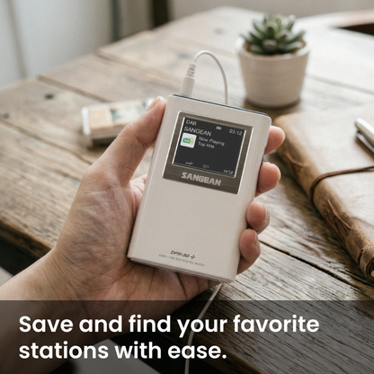 A hand holds a white Sangean portable digital audio player with a screen, connected to a white cable, in a rustic wooden setting with a small potted succulent in the background.