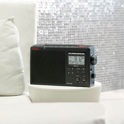Black radio with digital display on a white surface with a decorative background