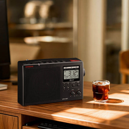 Black radio receiver on a wooden table with a glass of iced coffee in a blurred kitchen background
