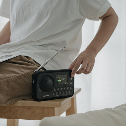 Person holding a black Samsung portable radio on a wooden stool.