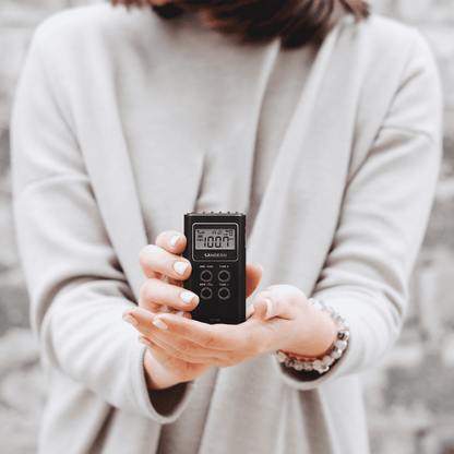 Person holding a black Sangean DT-120 AM/FM Stereo Pocket Radio with a blurred background