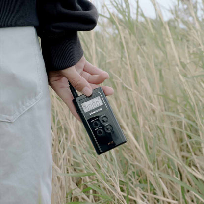 Person holding a Sangean DT-120 AM/FM Stereo Pocket Radio in a grassy outdoor setting