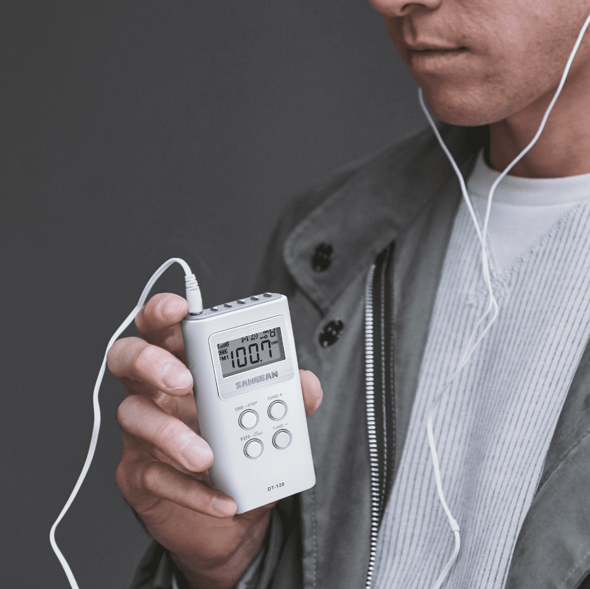 Person holding a digital device with earphones, against a dark background