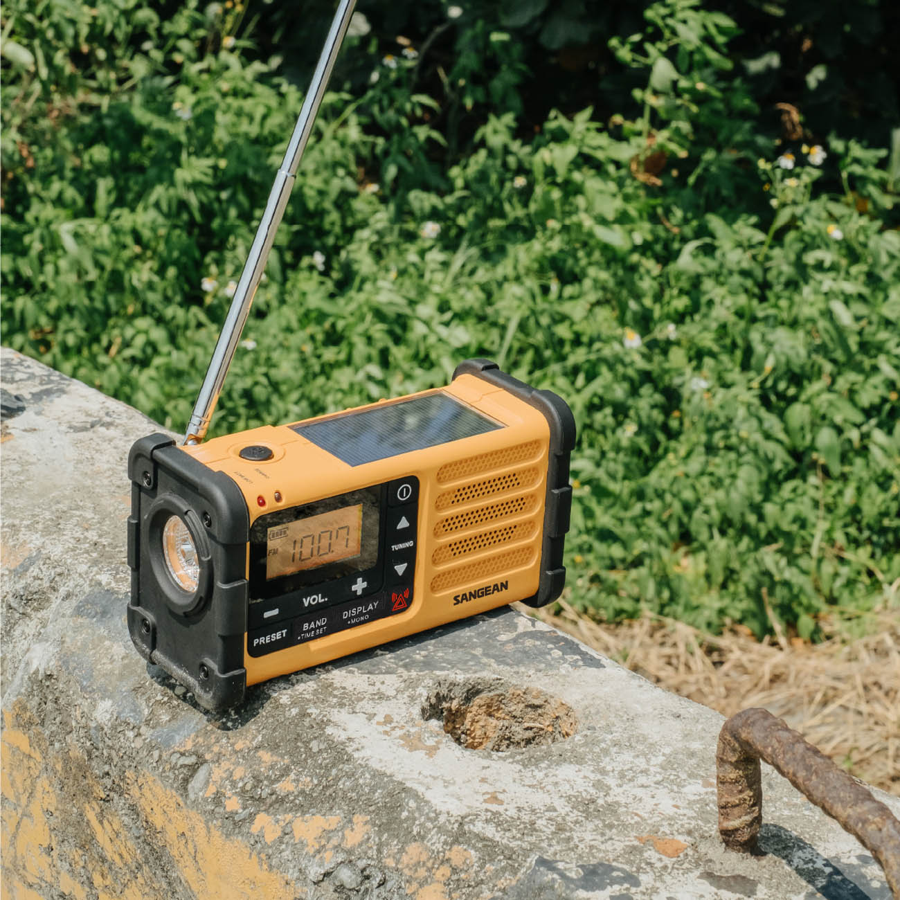 Sangean MMR-88 Emergency Radio on a stone surface with greenery in the background
