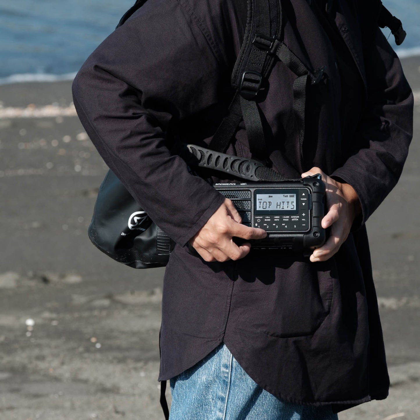 Person holding a black radio receiver with a digital display outdoors.