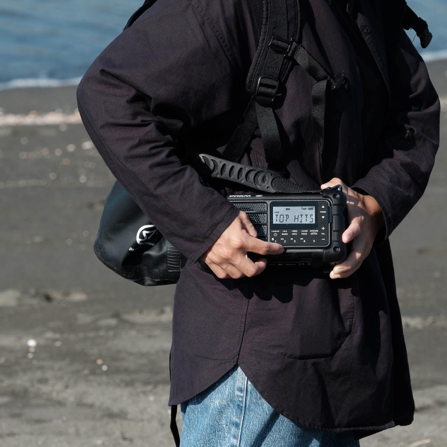 Person holding a black radio receiver with a digital display outdoors.