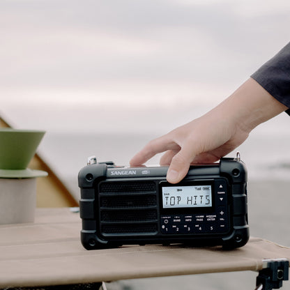 Person adjusting a Sangean radio on a table with a blurred background