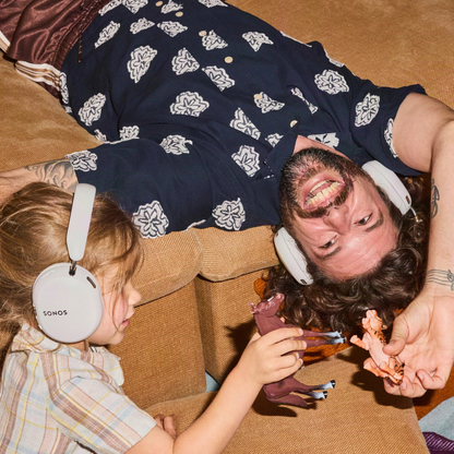 A man and a child wearing white over-ear headphones play with small figurines on a brown couch.