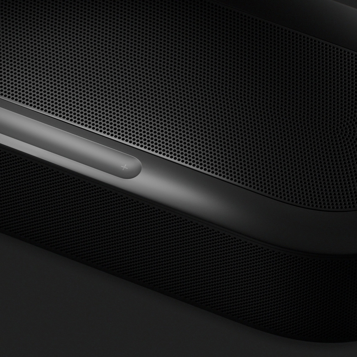 Close-up of a dark gray and black electronic device with a perforated metal grille and a glossy control strip.