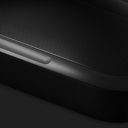 Close-up of a dark gray and black electronic device with a perforated metal grille and a glossy control strip.