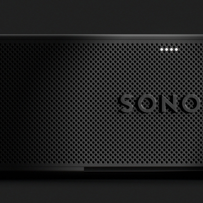 Close-up of a black Sonos speaker front grille with the embossed SONO logo and four small illuminated indicator lights, shown against a dark background.