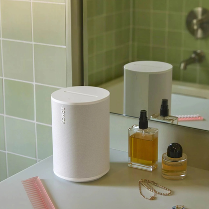 White Sonos ERA 100 on a bathroom counter with a mirror and toiletries in the background