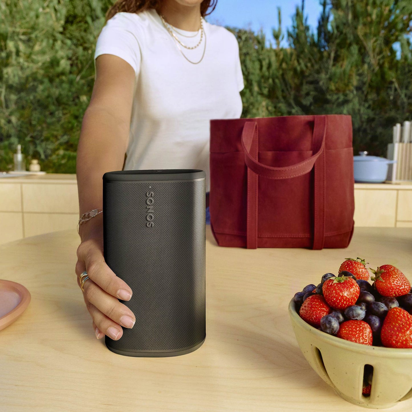 Person holding a black Sonos Play next to a bowl of fruits on a kitchen counter