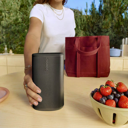 Person holding a black Sonos Play next to a bowl of fruits on a kitchen counter