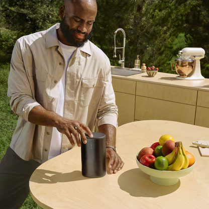 Man using Sonos Play at an outdoor kitchen table with a bowl of fruit.