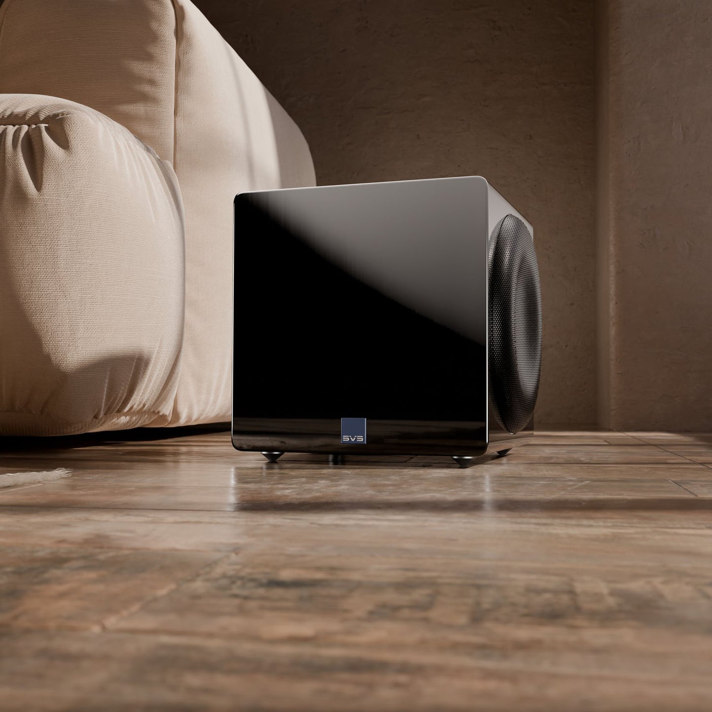 Black subwoofer on a wooden floor with a beige sofa in the background