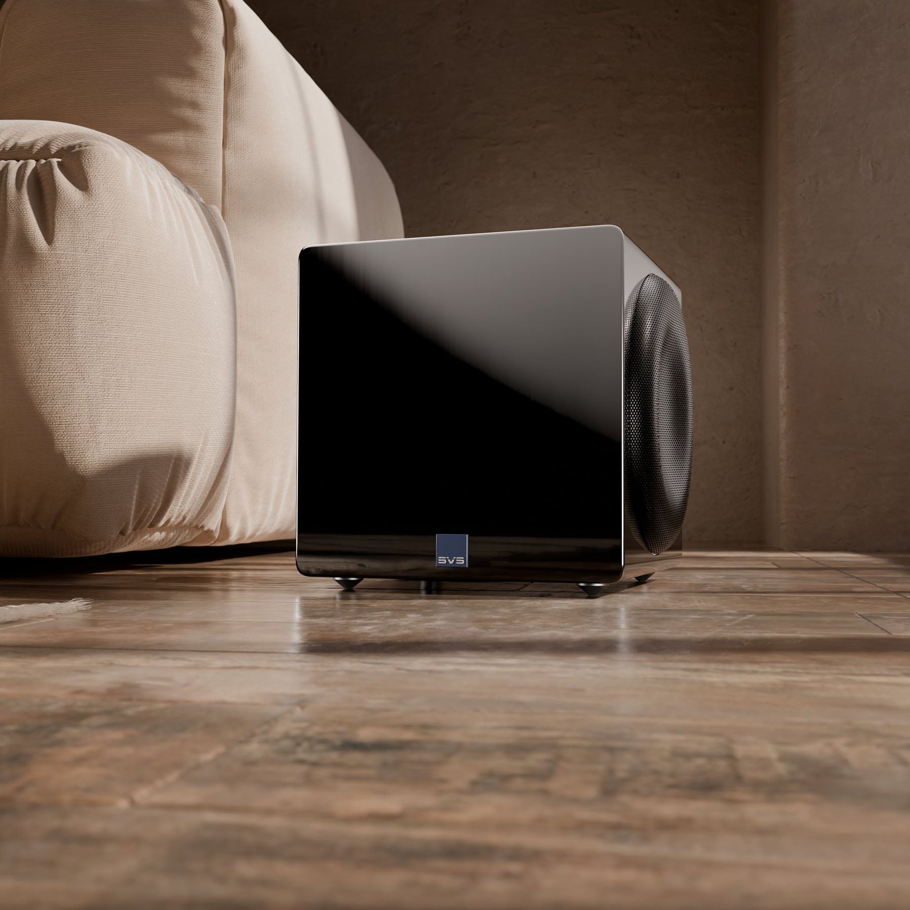 Black subwoofer on a wooden floor with a beige sofa in the background