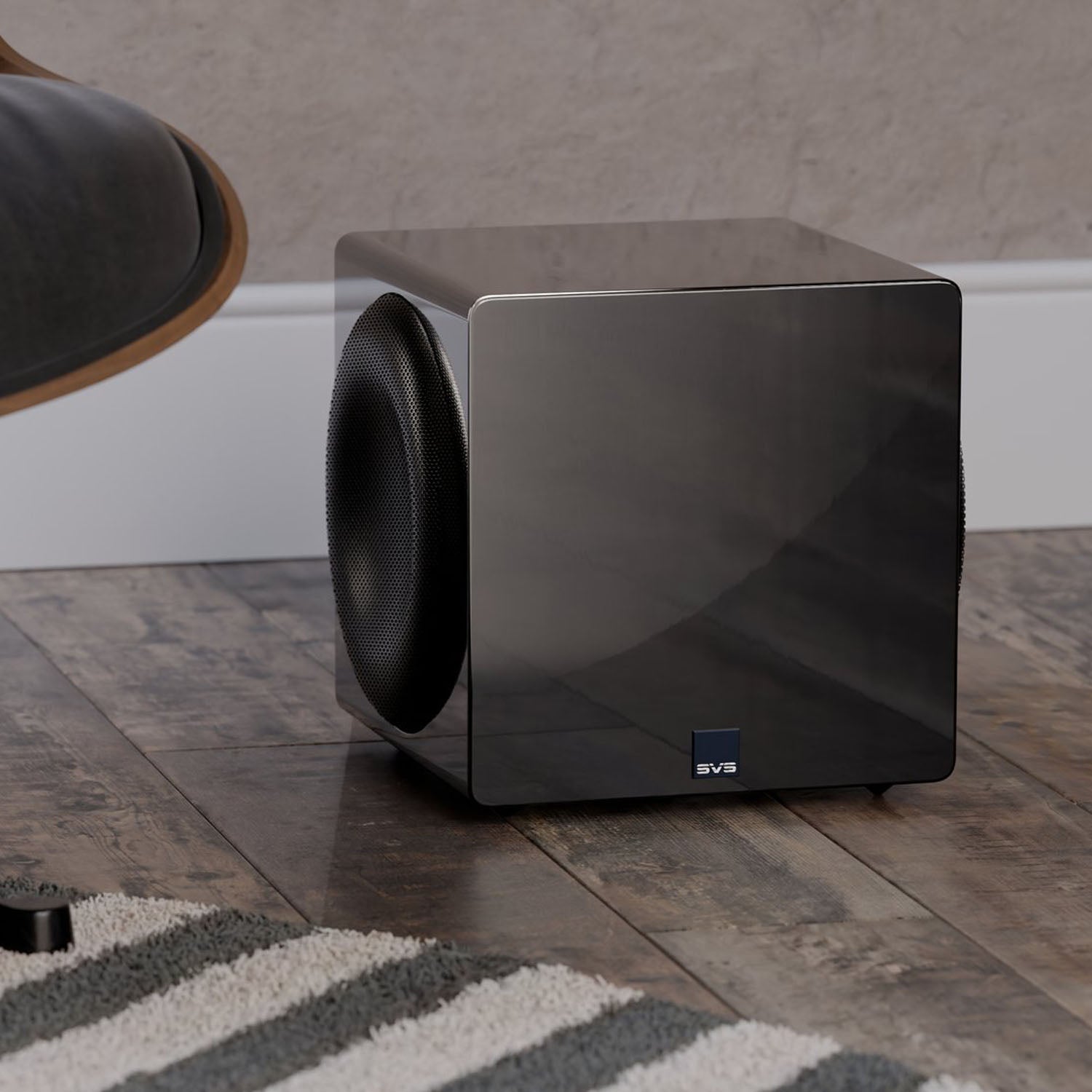 Black subwoofer on a wooden floor with a blurred chair in the background