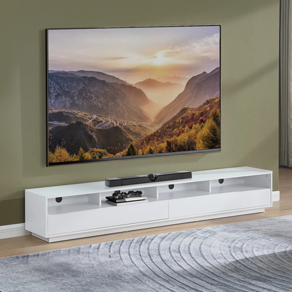A modern white TV cabinet with open shelving and a central drawer, styled in a living room setting below a large wall-mounted television displaying a mountain landscape. 