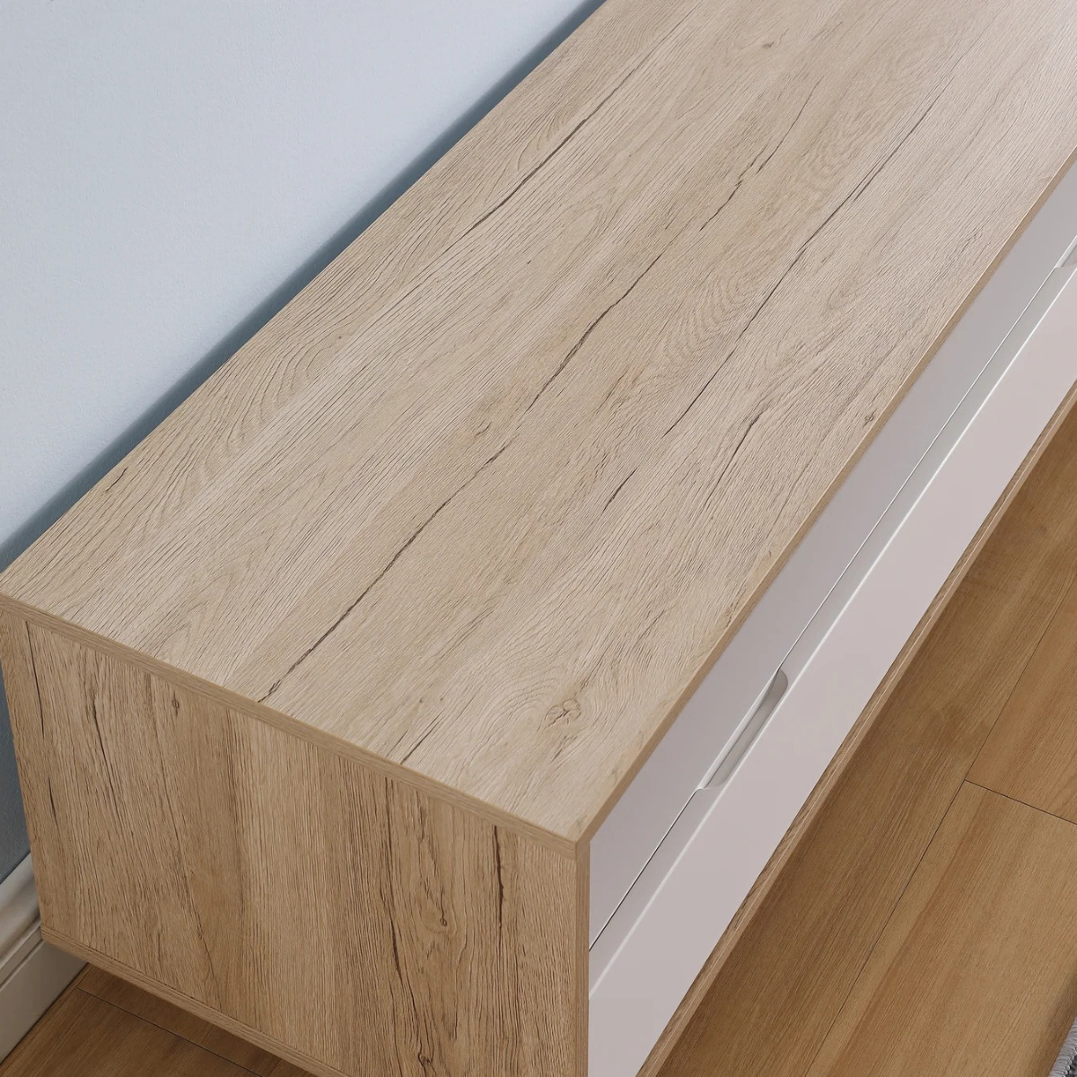 A close-up of a modern low cabinet or TV stand with a light oak wood grain top and side panel, paired with white drawer fronts and a light wood floor.