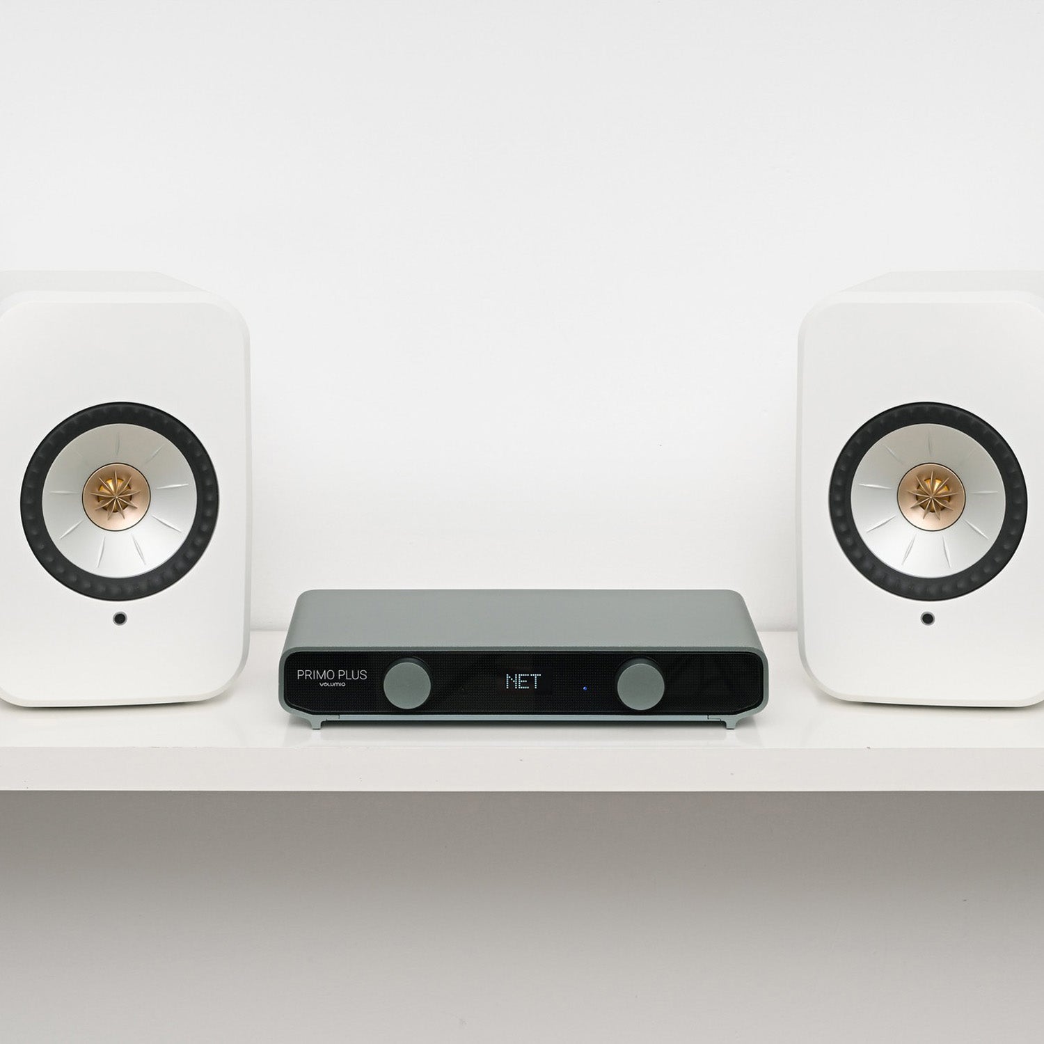 Two white speakers with a black audio receiver on a white shelf