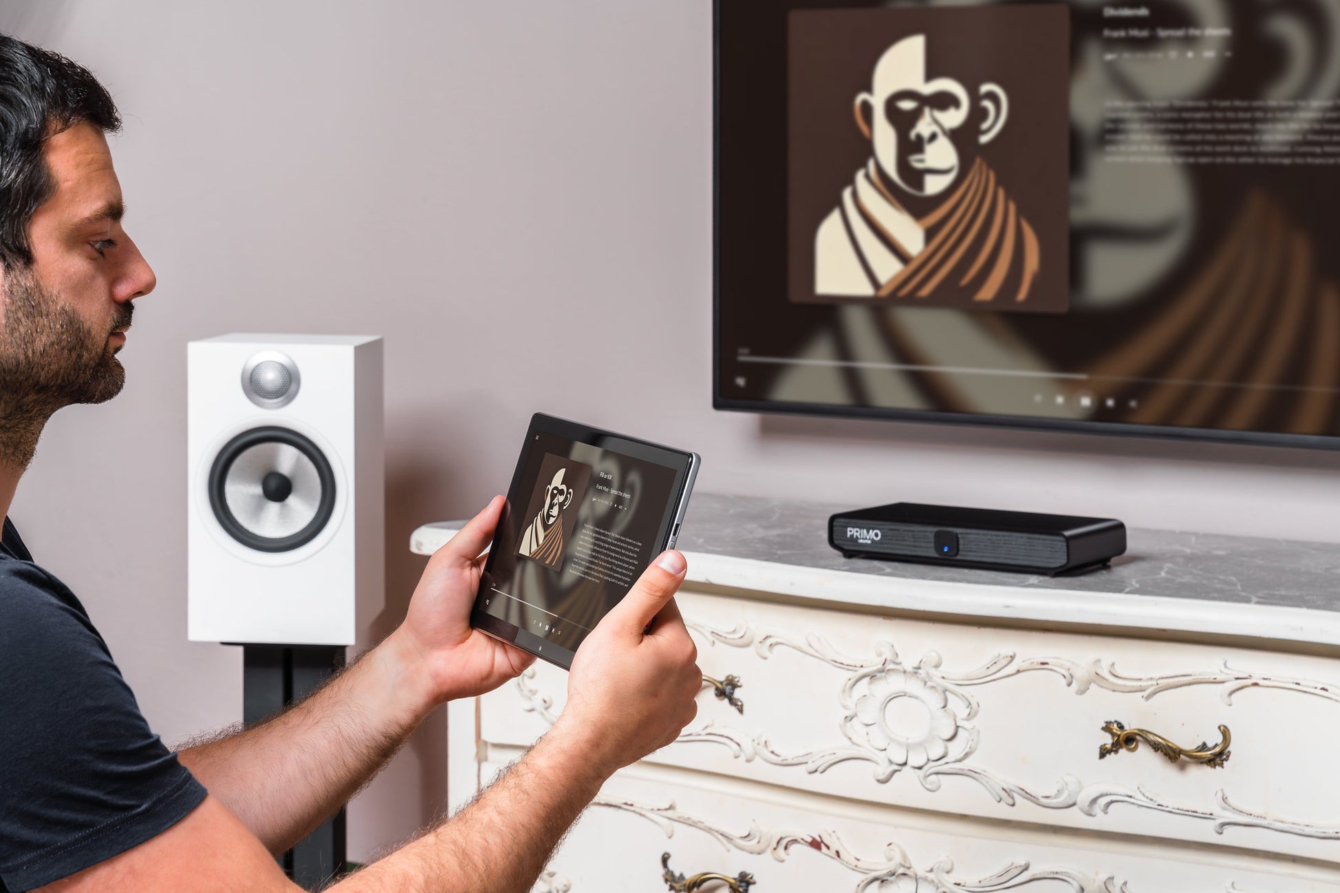 A man holds a tablet showing a projected image onto a wall-mounted screen above a white ornate cabinet, with a black projector on the cabinet and a white speaker beside him.