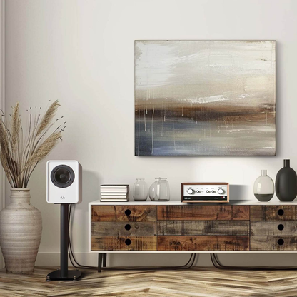 An abstract landscape painting with beige, brown, and blue tones hangs on a light wall above a rustic wooden console table styled with books, glass jars, a white speaker, and decorative vases.