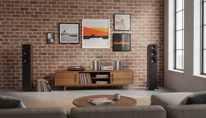 Modern living room with wooden entertainment console, speakers, and framed artwork on a brick wall.