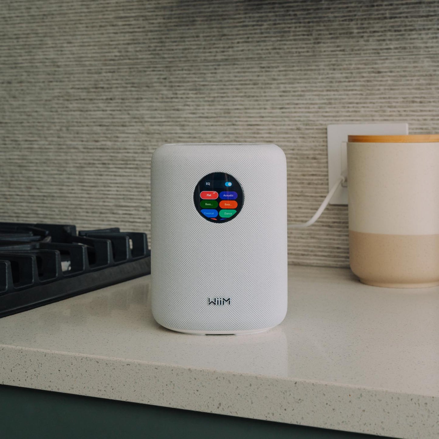 White WiiM Sound Smart Speaker on a desk with a keyboard and lamp in the background
