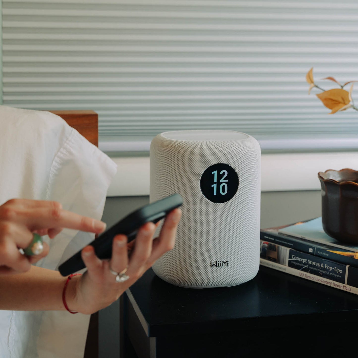 Person using a smartphone next to a white WiiM Sound Smart Speaker on a table with a blurred background