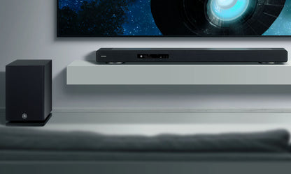 Soundbar system with subwoofer on a shelf in front of a television displaying a space-themed wallpaper.